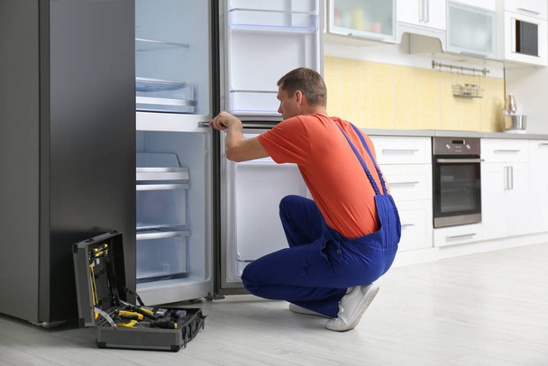 Male technician with screwdriver repairing refrigerator in kitchen - Valokuva, kuva