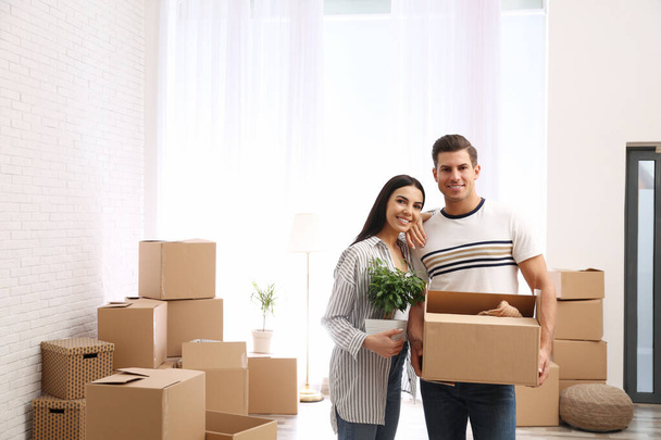 Happy couple in room with cardboard boxes on moving day - Foto, imagen