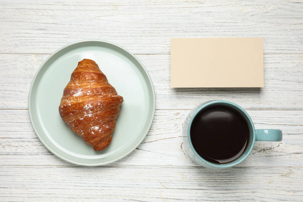 Croissant, coffee and blank card on white wooden table, flat lay. Tasty breakfast - Фото, изображение