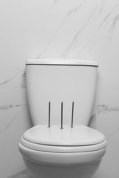 Toilet bowl with nails near marble wall. Hemorrhoids concept - Foto, afbeelding