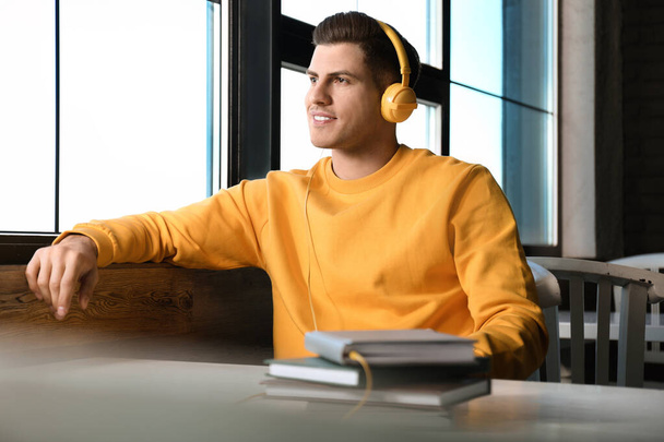 Man with headphones connected to book at table in cafe - Foto, Imagem