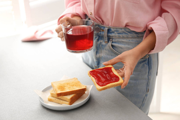 Woman having tasty breakfast with toast and raspberry tea at home, closeup. Morning routine - 写真・画像