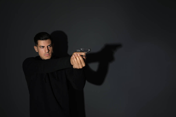 Professional killer with gun on black background - Фото, зображення
