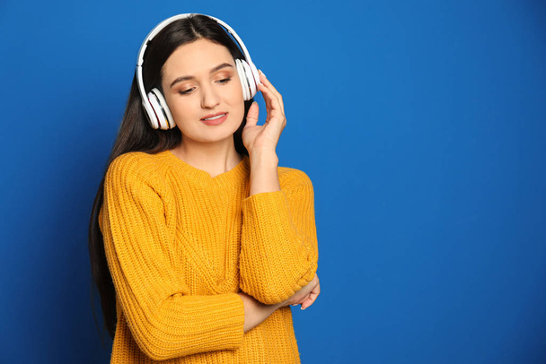 Young woman listening to audiobook on blue background. Space for text - Фото, изображение