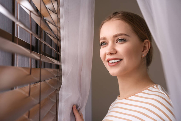 Vrouw bij raam met mooie gordijnen thuis - Foto, afbeelding