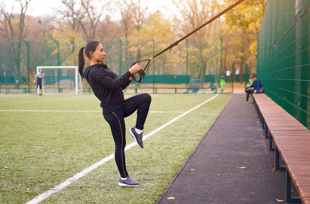 Girl athlete functional training on sportground. Mixed race young adult woman do workout with suspension system. Healthy lifestyle. Stretching outdoors playground. - Fotoğraf, Görsel