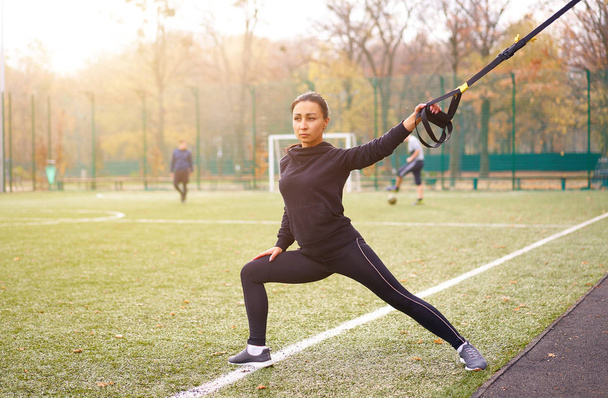 Girl athlete functional training on sportground. Mixed race young adult woman do workout with suspension system. Healthy lifestyle. Stretching outdoors playground. - Foto, immagini