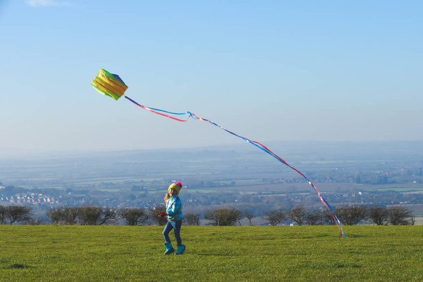Child flying a kite outdoors on a sunny clear day in a country f - Foto, imagen