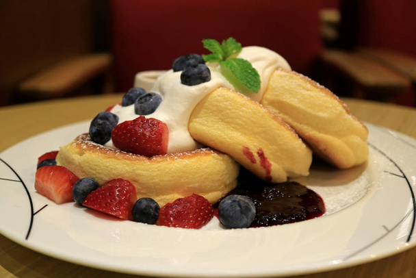 ホワイトプレートで提供される新鮮なホイップクリームとミックスベリーとふわふわのスフレパンケーキを加熱 - 写真・画像