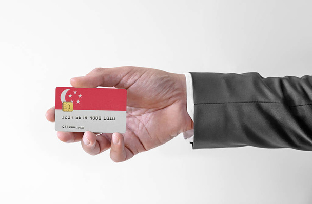 Bank credit plastic card with flag of Singapore holding man in elegant suit  - Foto, Imagen