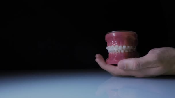 Close-up van tanden met transparante beugels. Demonstratie van de kaak met beugels in de hand van de arts. - Video