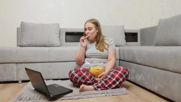 Chica con sobrepeso come patatas fritas y mira la pantalla del ordenador portátil
 - Imágenes, Vídeo