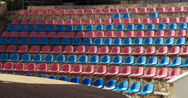 leerer Zuschauerraum im Freien. Halbrunde Plastikstühle sind von unten nach oben in Reihen angeordnet. farbenfroher Theaterhintergrund. - Foto, Bild