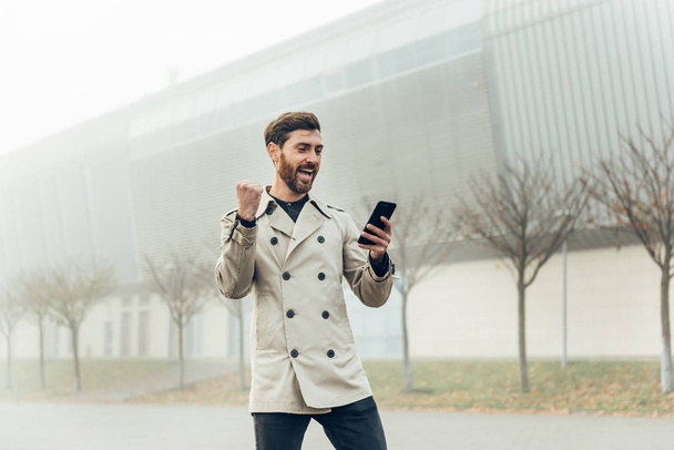 Excited handsome businessman cheering while receiving good news on phone. - Photo, Image