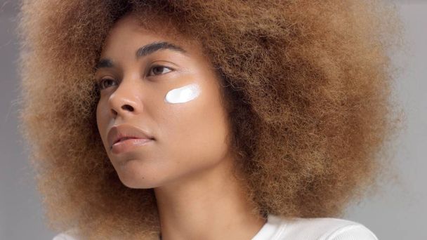 Gemengde race zwarte vrouw met grote afro haar in de studio zet een crème vlek - Foto, afbeelding