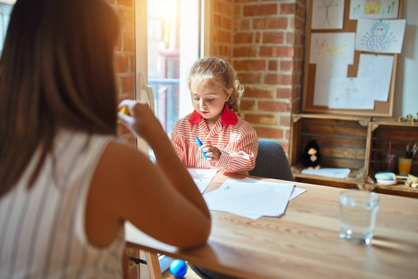 Όμορφη δασκάλα και ξανθιά μαθήτρια νήπιο κορίτσι φορώντας σχολική στολή σχέδιο χρησιμοποιώντας χρωματιστά στυλό στο νηπιαγωγείο - Φωτογραφία, εικόνα