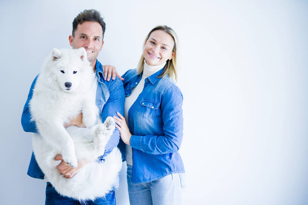 Young beautiful couple holding dog standing over isolated white background - Φωτογραφία, εικόνα
