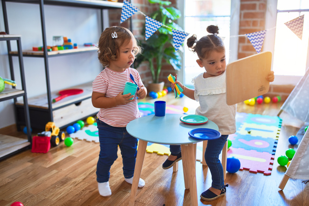 Очаровательные малыши, играющие в детские сады на пластиковой пище и столовых приборах
 - Фото, изображение
