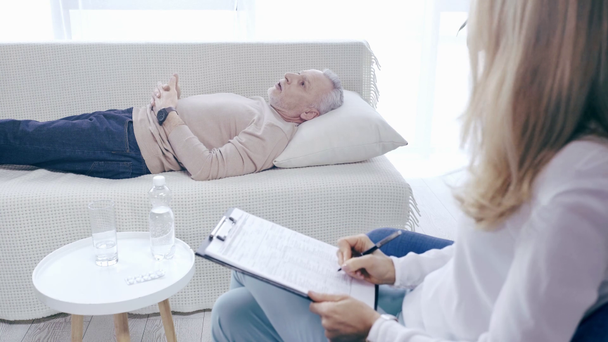 mature man lying on couch and talking to psychologist writing prescription - Footage, Video