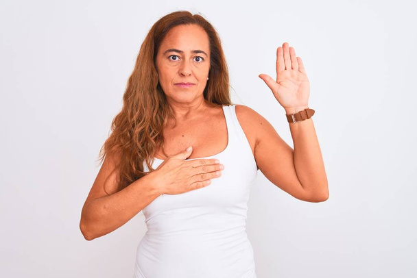 Mujer madura de mediana edad de pie sobre fondo blanco aislado Juramento con la mano en el pecho y la palma abierta, haciendo una promesa de lealtad juramento
 - Foto, imagen