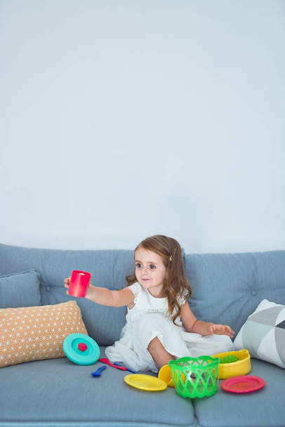 Adorable blond tout-petit assis sur le canapé cuisine avec de la nourriture et des couverts jouets à la maison
 - Photo, image