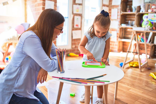 Caucasian girl kid playing and learning at playschool with female teacher. Mother and daughter at playroom around toys drawing on magnetic blackboard - Photo, Image