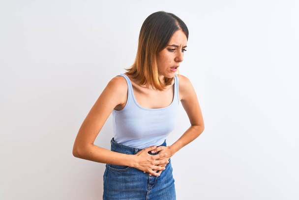 Beautiful redhead woman standing over isolated background with hand on stomach because indigestion, painful illness feeling unwell. Ache concept. - Photo, Image