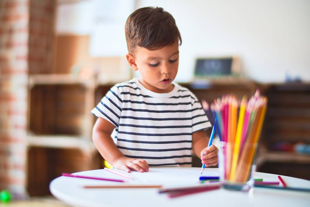 Gyönyörű kisgyermek fiú rajz aranyos sorsolás segítségével színes ceruzák óvodában - Fotó, kép