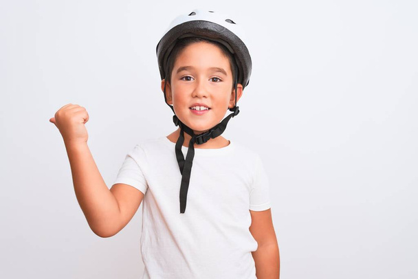 Mooie jongen dragen fiets security helm staan over geïsoleerde witte achtergrond glimlachen met gelukkig gezicht kijken en wijzen naar de zijkant met duim omhoog. - Foto, afbeelding