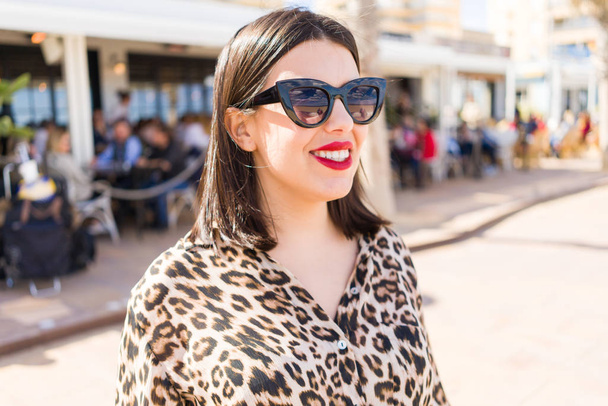 Joven hermosa mujer con labios rojos con gafas de sol sonriendo feliz en la calle
 - Foto, Imagen