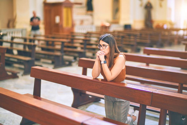 Young beautiful woman praying on her knees in a bench at church - Foto, Imagen