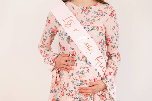 Young pregnant woman with a dress and a pink scarf puts her hand - Foto, afbeelding
