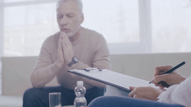 mature patient talking to psychologist writing on clipboard - Кадри, відео