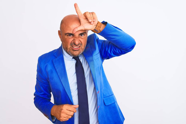 Middle age businessman wearing suit standing over isolated white background making fun of people with fingers on forehead doing loser gesture mocking and insulting. - Photo, Image