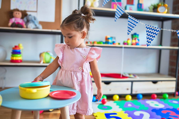 Fiatal gyönyörű kisgyermek játszik evőeszközök és élelmiszer játékok az asztalon kindergaten - Fotó, kép