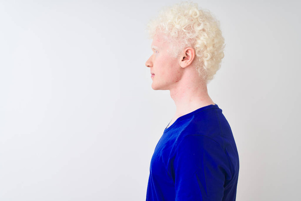 Mavi günlük tişört giyen genç albino bir adam izole edilmiş beyaz arka plan üzerinde duruyor, yan tarafa bakıyor, rahat bir poz veriyor kendine güvenen bir gülümsemeyle doğal bir yüz ifadesi sergiliyor.. - Fotoğraf, Görsel