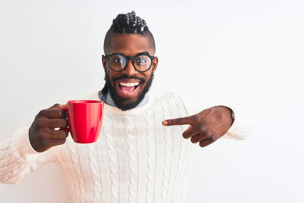 Afro-Amerikaanse man met vlechten drinken kopje koffie over geïsoleerde witte achtergrond met verrassingsgezicht wijzend vinger naar zichzelf - Foto, afbeelding