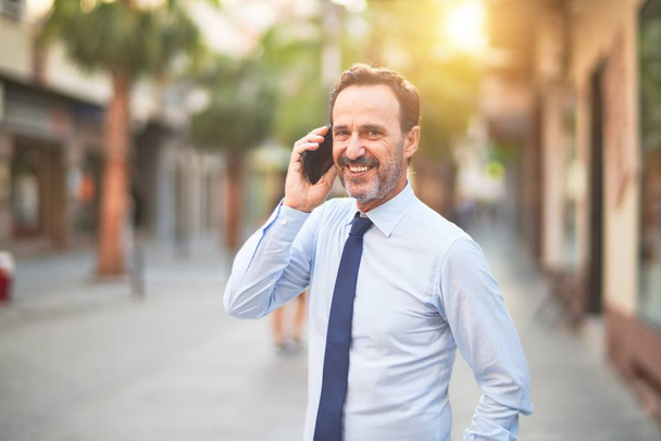 Middle age handsome businessman talking on the smartphone smiling - Photo, image