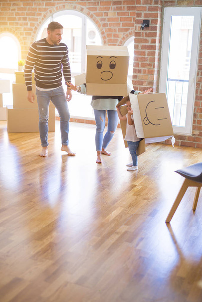 Bela famiily com criança brincando com caixas de fanny de papelão em nova casa
 - Foto, Imagem