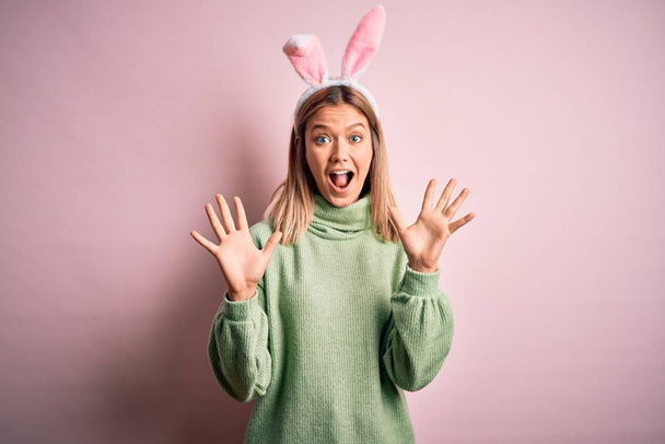 Mujer hermosa joven con orejas de conejo de Pascua de pie sobre un fondo rosa aislado celebrando loco y sorprendido por el éxito con los brazos levantados y los ojos abiertos gritando emocionados. Concepto ganador
 - Foto, imagen