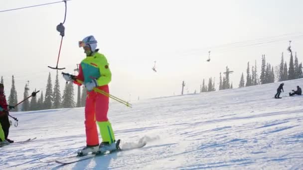 Stok narciarski. Narciarze i snowboardziści jeżdżą po torze. Narciarz wspina się na górę wyciągiem narciarskim. - Materiał filmowy, wideo