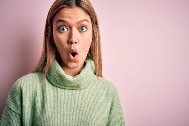 Young beautiful blonde woman wearing winter wool sweater over pink isolated background afraid and shocked with surprise expression, fear and excited face. - 写真・画像