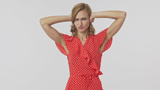 Displeased pretty blonde woman in dress doesn't want to hear anything and covering her ears while looking at the camera over grey background - Footage, Video