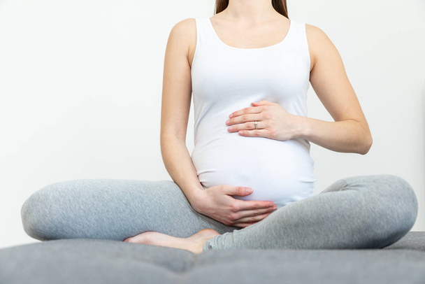 Mladá těhotná žena drží své břicho sedí na pohovce - Pohlaví  - Fotografie, Obrázek