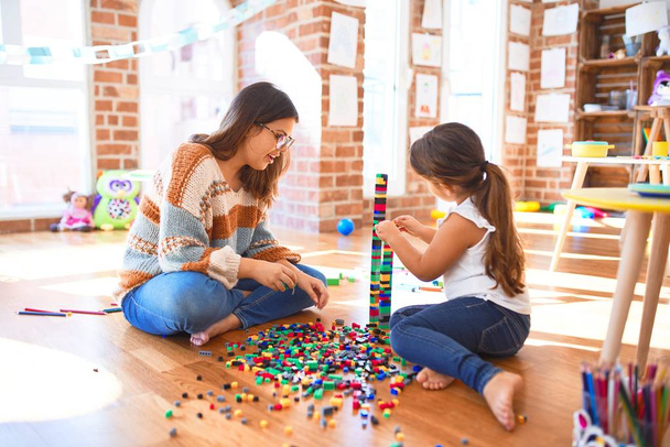 美しい先生と幼児は、幼稚園でおもちゃの多くの周りにブロックおもちゃを構築して遊んでいます - 写真・画像