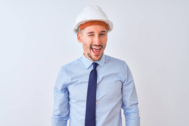 Young business man wearing contractor safety helmet over isolated background winking looking at the camera with sexy expression, cheerful and happy face. - Foto, immagini