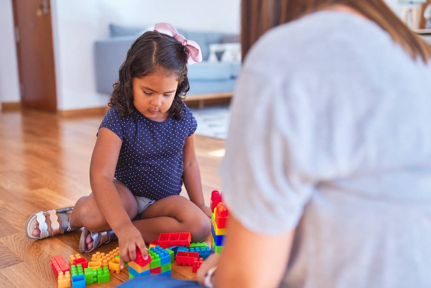 Beautiful teacher and toddler girl playing with construction blocks bulding tower at kindergarten - Photo, Image