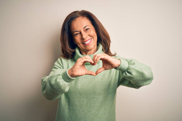 Middle age beautiful woman wearing casual turtleneck sweater over isolated white background smiling in love doing heart symbol shape with hands. Romantic concept. - Photo, Image