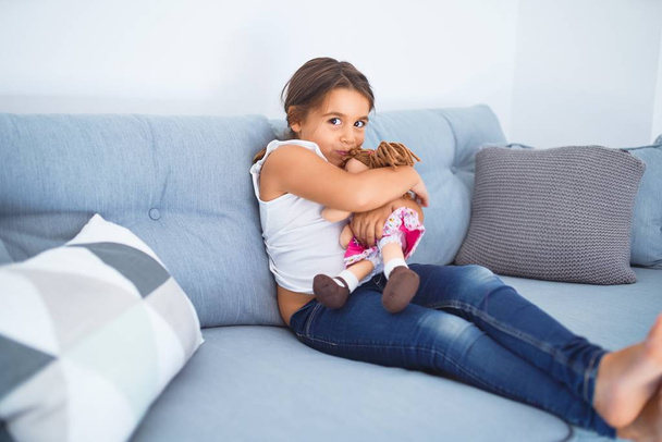 Adorable toddler smiling happy. Sitting on the sofa hugging doll at home - Foto, imagen