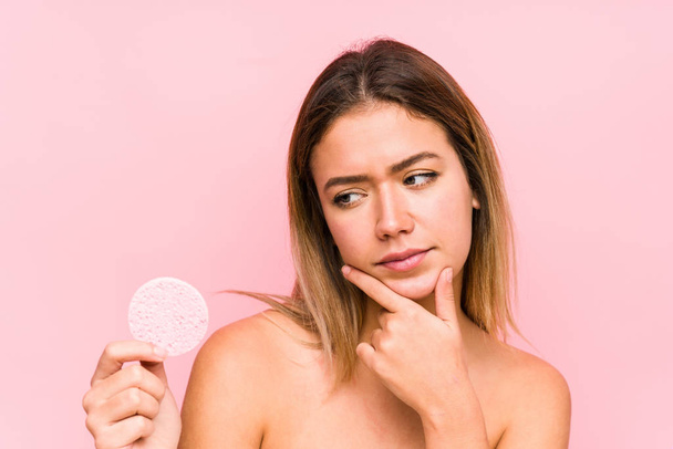 Young caucasian woman holding a facial disk isolated looking sideways with doubtful and skeptical expression. - Foto, Bild